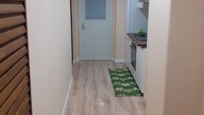 A narrow hallway with wooden flooring, a white door at the end, and a small kitchen area with a green mat. - Piazza Roma holidays House  (Catania)