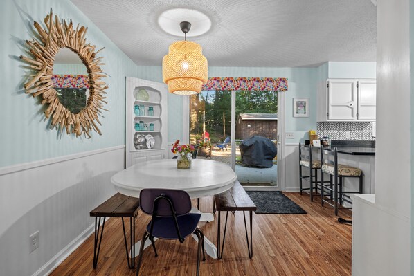 A dining area with a round table, chairs, a hanging light fixture, and a decorative mirror on the wall.