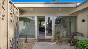 A modern house with a patio area featuring a glass door entrance, a small table, and a cactus plant. - Mid Century Modern-Stunning Mountain Views, Quiet, Clean, Bright & Open Design. (Indian Wells)
