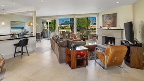 A modern living room with a fireplace, a dining area, and a large window overlooking a garden. - Mid Century Modern-Stunning Mountain Views, Quiet, Clean, Bright & Open Design. (Indian Wells)