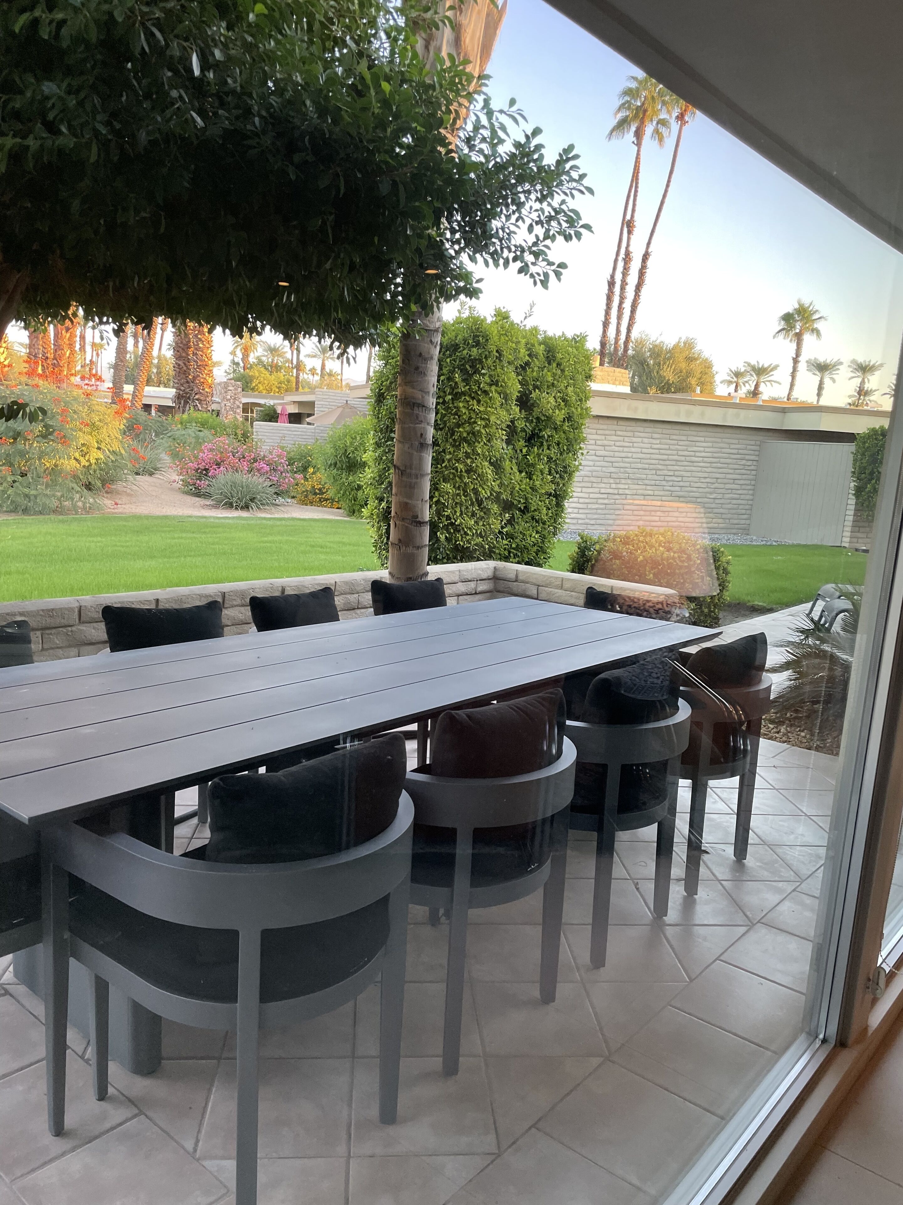 Une terrasse extérieure avec une table rectangulaire et des chaises, entourée d’une structure vitrée.