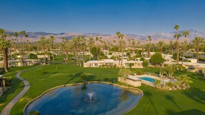 A golf course with a pond, palm trees, and mountains in the background. - Mid Century Modern-Stunning Mountain Views, Quiet, Clean, Bright & Open Design. (Indian Wells)
