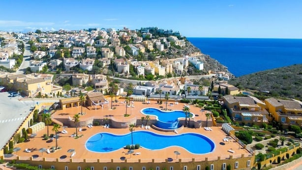 A coastal resort with a large swimming pool, terraced buildings, and a clear view of the sea. - Apartamento Jardines PG018 - Benitachell, Costa Blanca (Benitachell)