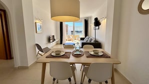 A dining area with a table set for four, a hanging light fixture, and a view of the balcony. - Apartamento Jardines PG018 - Benitachell, Costa Blanca (Benitachell)