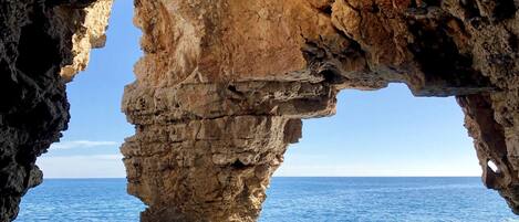 A natural rock formation with a cave-like opening, overlooking the sea.