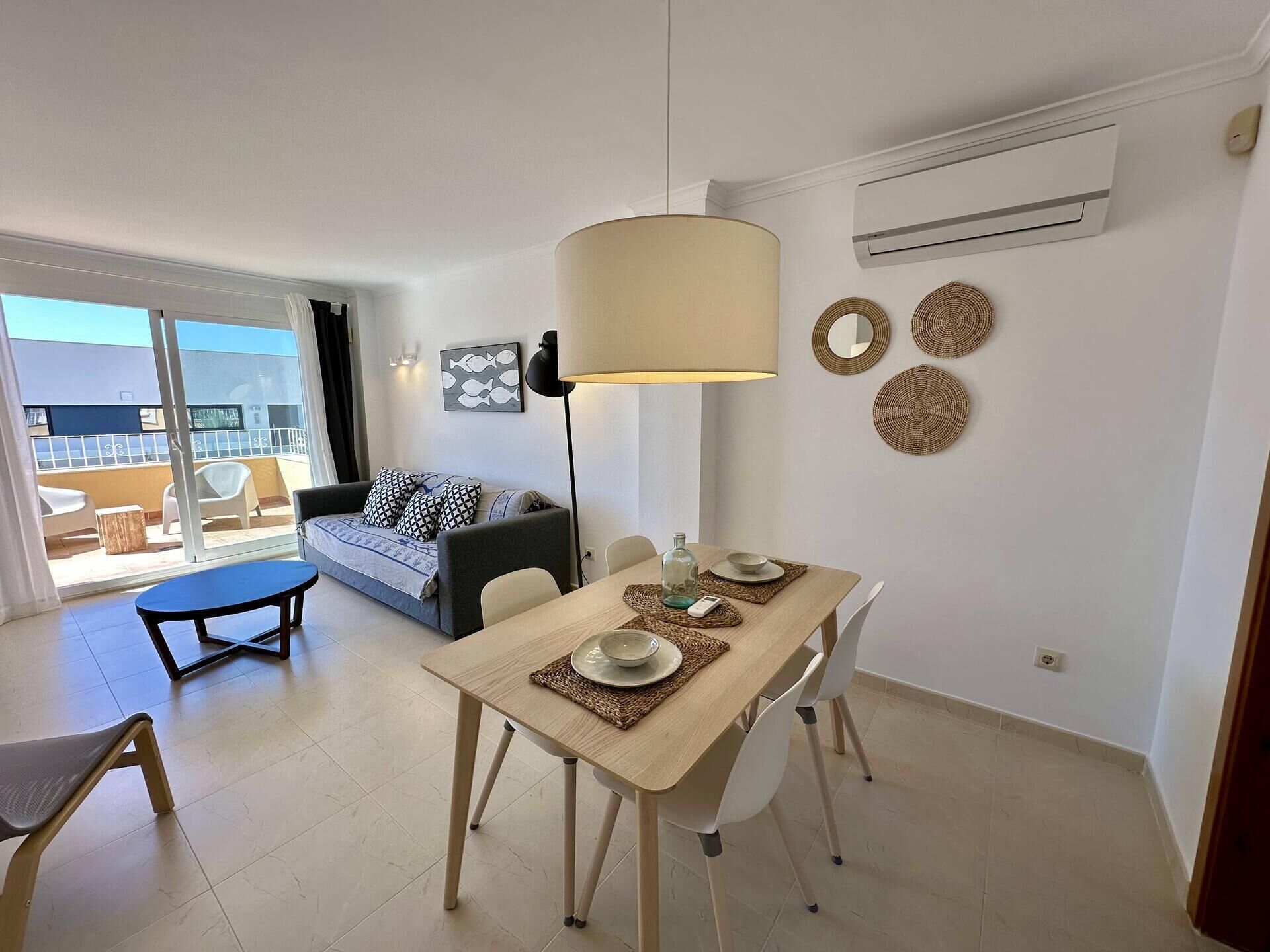 A modern living room with a dining area, a sofa, a coffee table, and a balcony with outdoor furniture.
