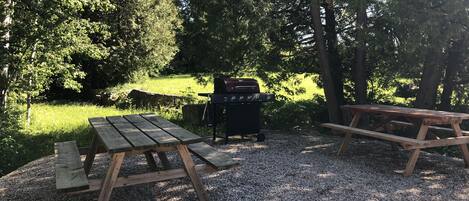 An outdoor picnic area with two wooden picnic tables and a barbecue grill.