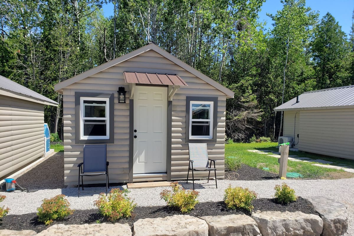Une petite cabane d’un seul étage, avec une porte d’entrée, deux fenêtres et une véranda équipée de deux chaises.