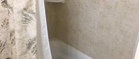 Un baño con bañera, paredes de azulejos y cortina de ducha estampada con motivos florales.