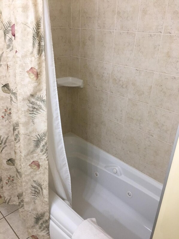 Un baño con bañera, paredes de azulejos y cortina de ducha estampada con motivos florales.