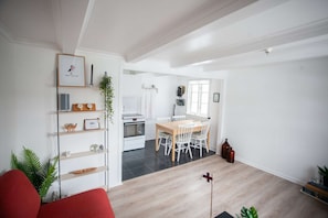 Una sala moderna con un sofá rojo, un comedor con mesa y sillas de madera, una cocina con electrodomésticos blancos y una pequeña bandera en el suelo.