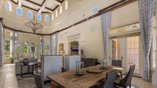 A spacious dining area with a wooden table and wicker chairs, a chandelier, and a view of the outdoors through large windows. - Great View Condo, 2 Min. from Disney World!- 70 (Orlando)