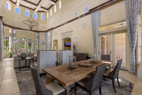 A spacious dining area with a wooden table and wicker chairs, a chandelier, and a view of the outdoors through large windows.. Great View Condo, 2 Min. from Disney World!- 70