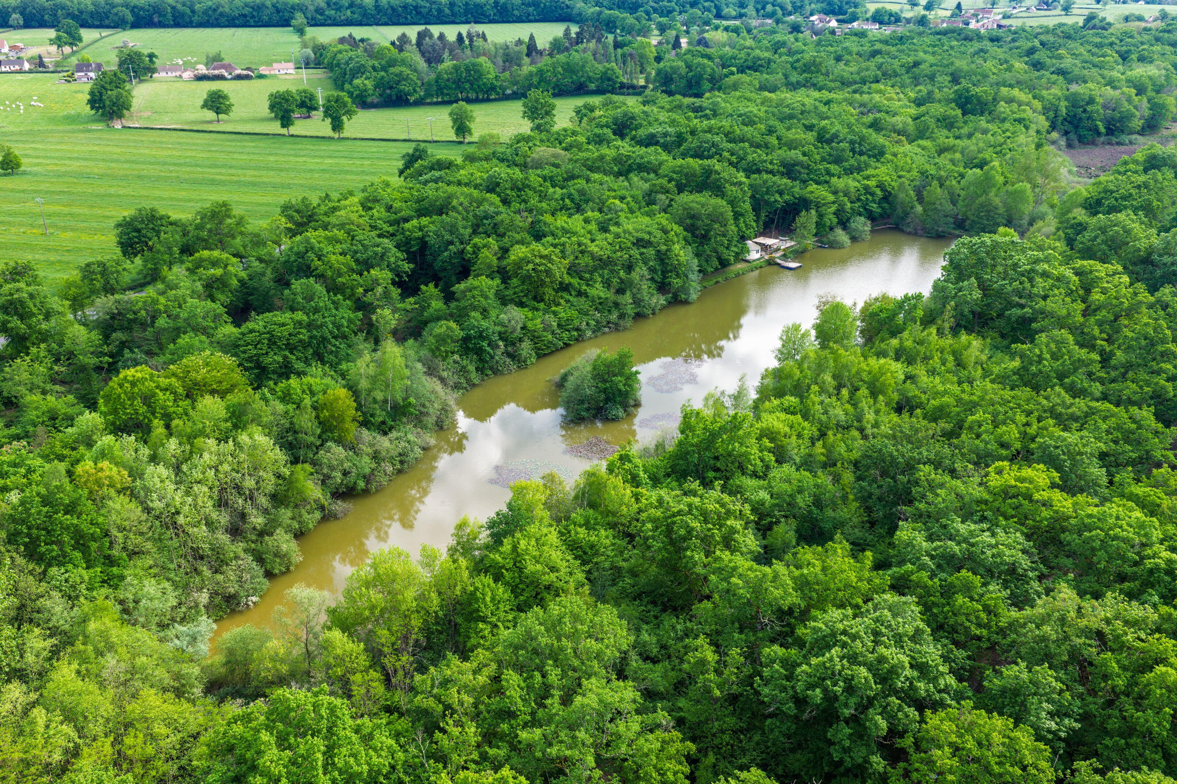 A river winding through a densely wooded area with a small building near the water's edge.