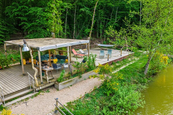 A wooden deck with outdoor furniture, a hammock, and a view of a river.