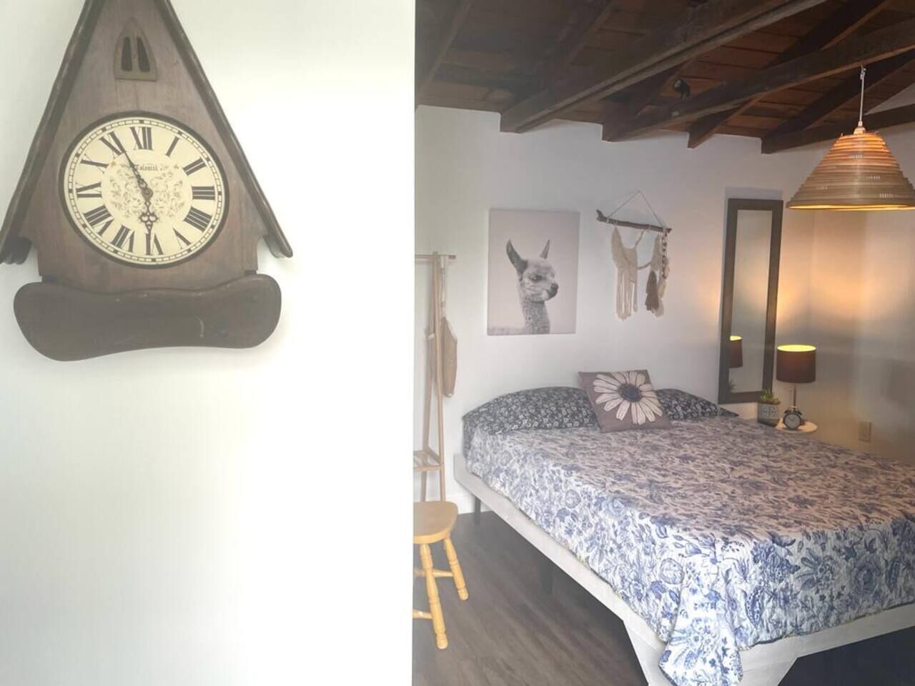 Una habitación con una cama, techo de madera, un reloj de pared y un cuadro enmarcado.