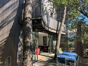 A modern outdoor seating area with a glass table and chairs, surrounded by trees and a wooden fence.