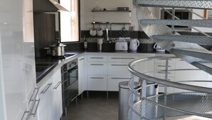 A modern kitchen with white cabinetry, stainless steel appliances, and a spiral staircase. - ECO-Responsible Treehouse / Welcome to Nature (Moliets-et-Maa)