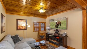 Un salon chaleureux avec un canapé d’angle, une cheminée, un plafond en bois et un tableau représentant un cheval en train de brouter.