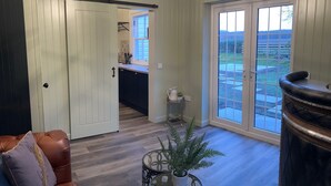 Una sala de estar con un sofá de cuero marrón, una mesa de centro de vidrio con una planta, un reposapiés de cuero negro y una puerta corrediza de vidrio que da a un patio trasero.