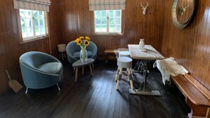 Una habitación con paredes de madera, una mesa de comedor, una silla azul, un taburete pequeño, un jarrón con flores y una cabeza de venado montada en la pared.