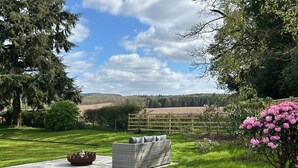 Un jardín con un hogar para fuego, un sofá de mimbre y vistas a un campo y colinas.