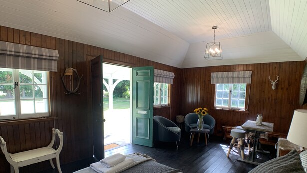 Una habitación acogedora con una cama, dos sillones, una mesita de noche con una lámpara y un ventanal con vistas al exterior.