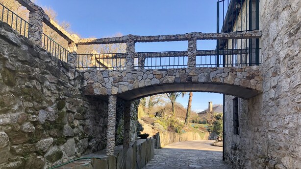 A stone bridge over a narrow stone pathway leading to a building with a stone facade.
