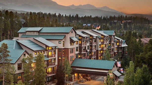 A multi-story hotel with a green roof, surrounded by trees and mountains in the background. - SPRING BREAK Two-Bedroom Condo in Breck with private hot-tub! (Breckenridge)