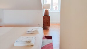 Une chambre à coucher avec un lit, une table de chevet avec une lampe, et une vue sur l’extérieur par une fenêtre.