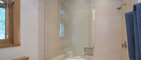 A modern bathroom with a glass-enclosed shower, a white bathtub, and a blue towel hanging on the wall.