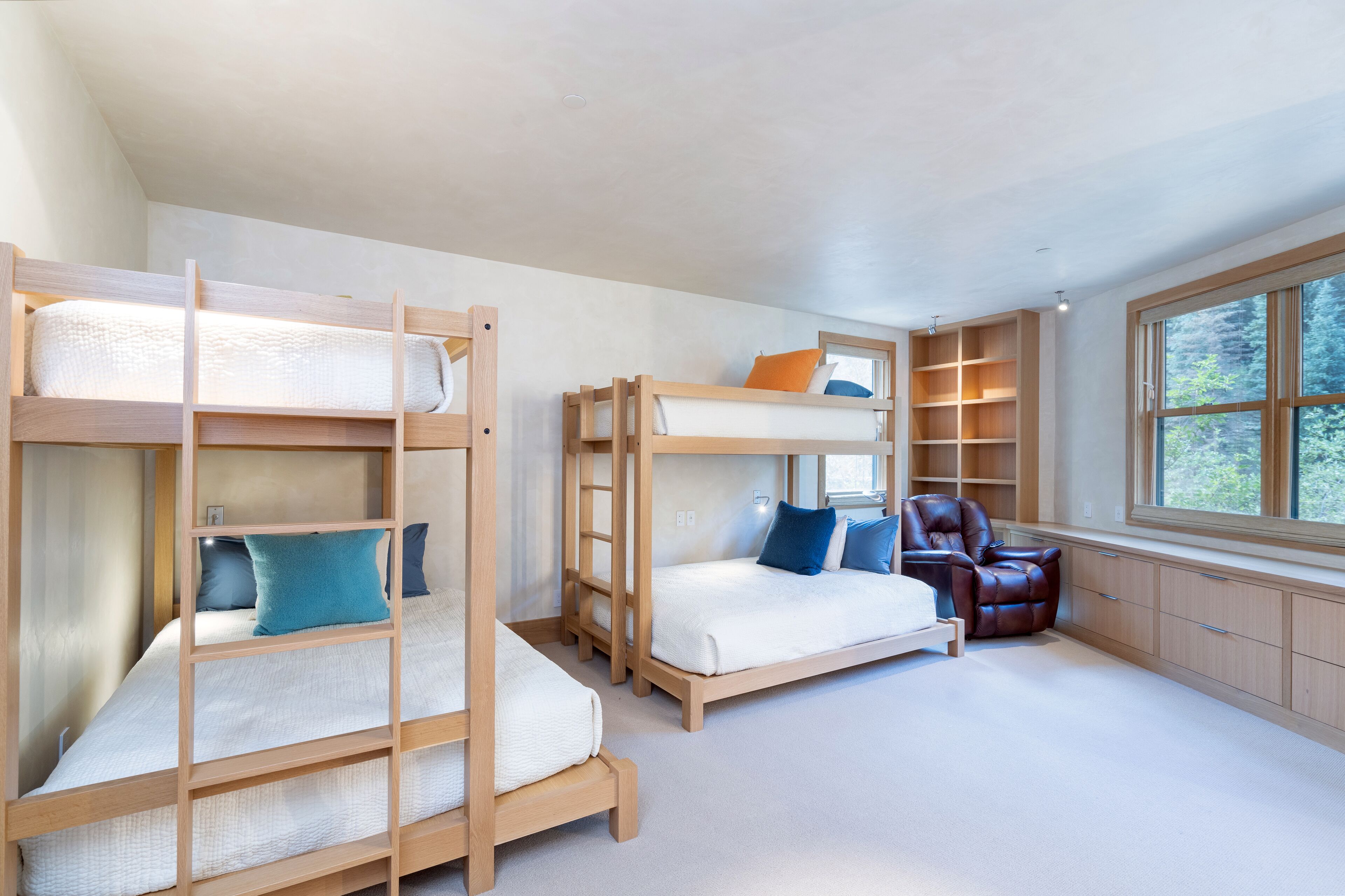 Une chambre avec des lits superposés, une chaise et des étagères intégrées.