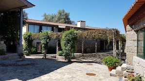 A courtyard with stone flooring, a stone wall, and a building with a tiled roof.