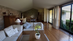 A spacious living room with a stone wall, a wooden sofa set, a dining table, and a potted plant.