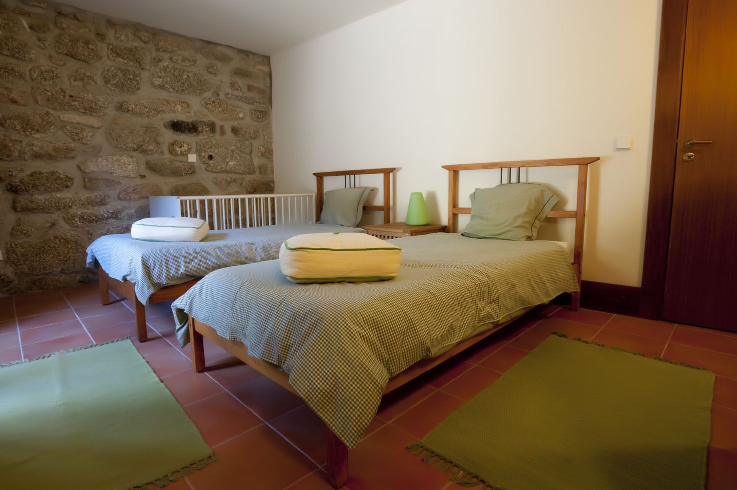 A room with two beds, a stone wall, a wooden door, and a tiled floor.