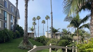 A pathway leading to a building with a modern design, surrounded by well-maintained greenery and palm trees. - Northcoast Village Beautiful Penthouse w/ large rooftop deck and VIEWS! (Oceanside)