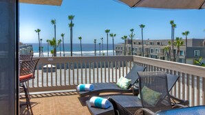 A balcony with wicker furniture, a view of the ocean, and palm trees. - Northcoast Village Beautiful Penthouse w/ large rooftop deck and VIEWS! (Oceanside)