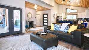 A spacious living room with a black leather sofa, a coffee table, and a dining area with a kitchen in the background.