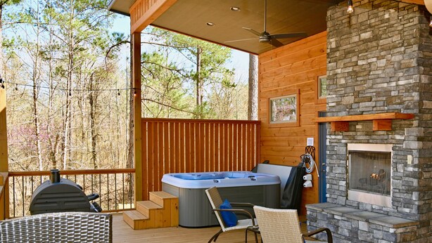 A wooden deck with a hot tub, wicker chairs, and a stone fireplace.