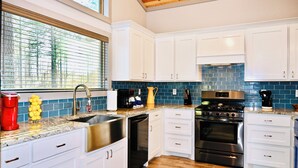 A modern kitchen with white cabinets, a stainless steel sink, a coffee maker, and a stove.