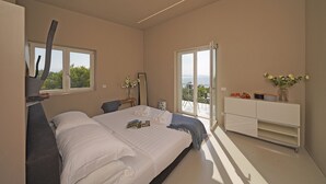 A modern bedroom with a large bed, a bedside table with a lamp, a dresser, and a view of the outdoors through a sliding door.