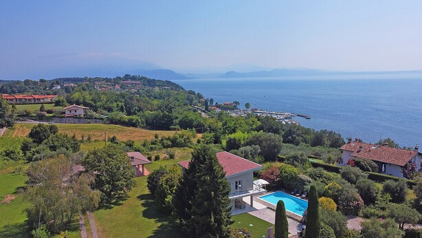 A residential property with a swimming pool, lush greenery, and a view of the sea and distant mountains.
