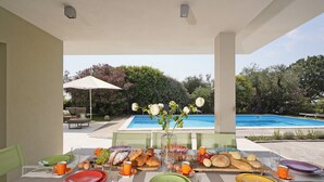 An outdoor dining area with a pool view, featuring a table set with plates, glasses, and food.