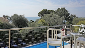 A poolside area with a view of the sea, surrounded by trees and a railing.