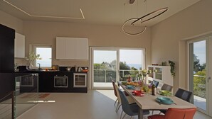 A modern kitchen with a dining area, large windows, and a view of the outdoors.