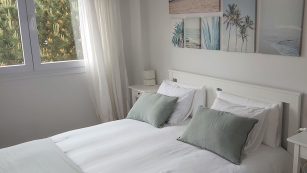 A neatly made bed with white linens and two green pillows, a white nightstand with a lamp, and a wall with framed artwork. - Apt. on Mataleñas Beach next to the golf course and Playas del Sardinero (Santander)