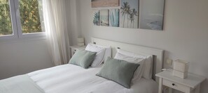 A neatly made bed with white linens and two green pillows, a white nightstand with a lamp, and a wall with framed artwork. - Apartment on Mataleñas Beach, next to the golf course and Playas del Sardinero (Santander)