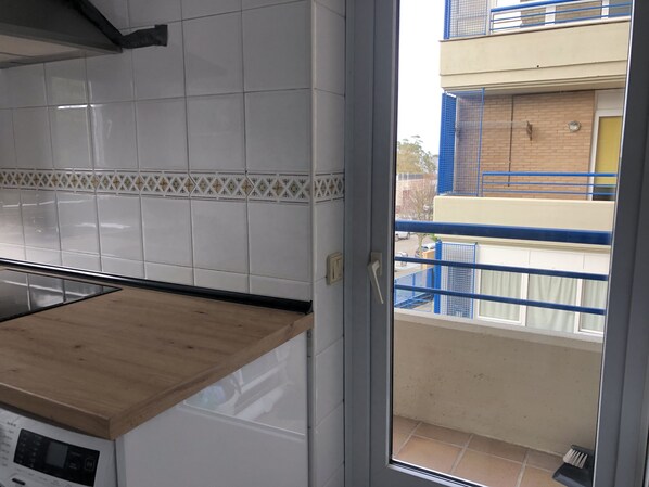 A kitchen with white tiles, a wooden countertop, and a view of a balcony with blue railings. - Apartment on Mataleñas Beach, next to the golf course and Playas del Sardinero (Santander)