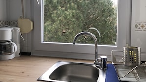 A kitchen with a stainless steel sink, a window with a view of trees, a coffee maker, and a dish rack. - Apt. on Mataleñas Beach next to the golf course and Playas del Sardinero (Santander)