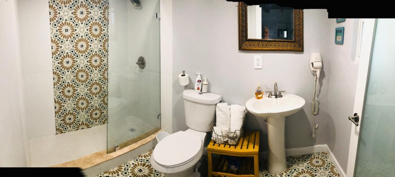 Un bagno con doccia vetrata, un water, un lavandino e un piccolo sgabello.